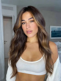 Young woman with long wavy brown hair and blonde highlights wearing a white crop top and cardigan indoors